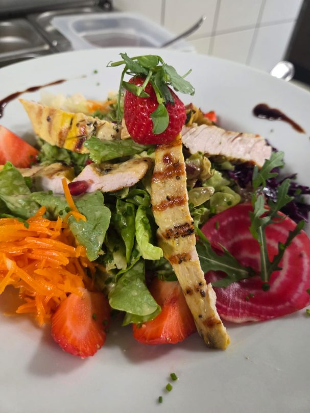 Bunte Salatplatte mit gegrilltem Hähnchen, Erdbeeren, Rote Bete und frischen Kräutern.