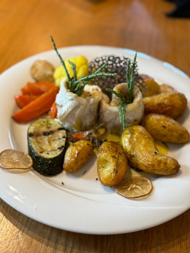 Teller mit gebratenem Gemüse, Kartoffeln und Fischröllchen, dekoriert mit Kräutern.