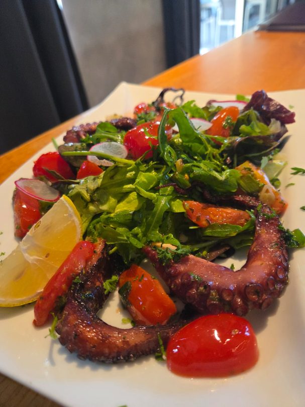 Gegrillter Oktopus auf einem Bett aus frischem Salat und Kirschtomaten, garniert mit Zitrone.