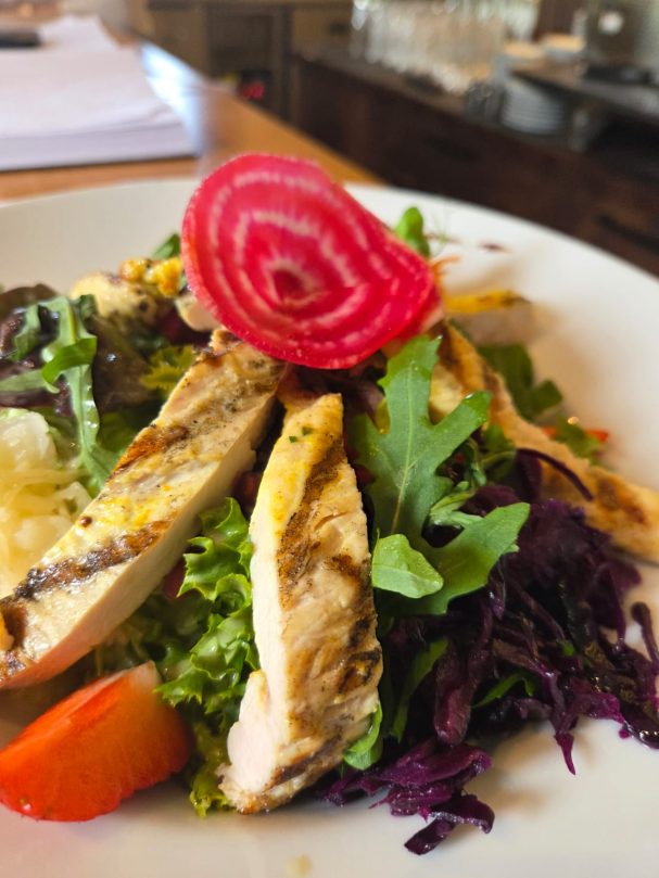 Gegrilltes Hähnchenfilet auf einem Bett aus buntem Salat mit Rote-Bete-Scheibe.