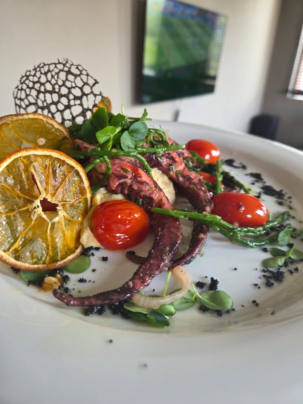 Gegrillter Oktopus mit Zitronenscheiben, Kirschtomaten und frischen Kräutern.